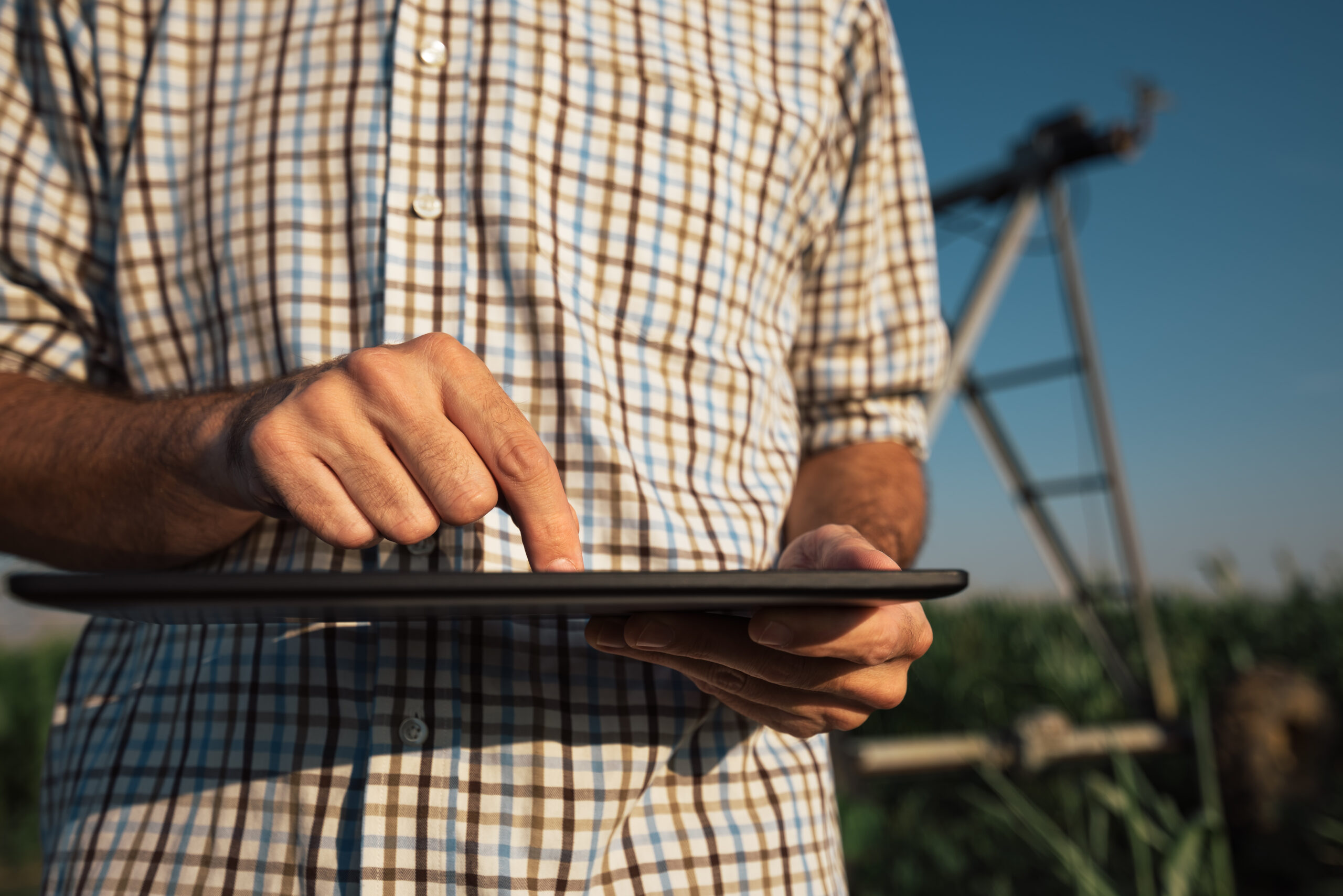 Serious concerned farmer using tablet computer in cornfield with irrigation system out of operation during warm summer day
